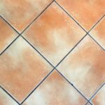 Fughe di piastrelle pulite e bianche grazie all'aceto, con panno e spugna in primo piano.